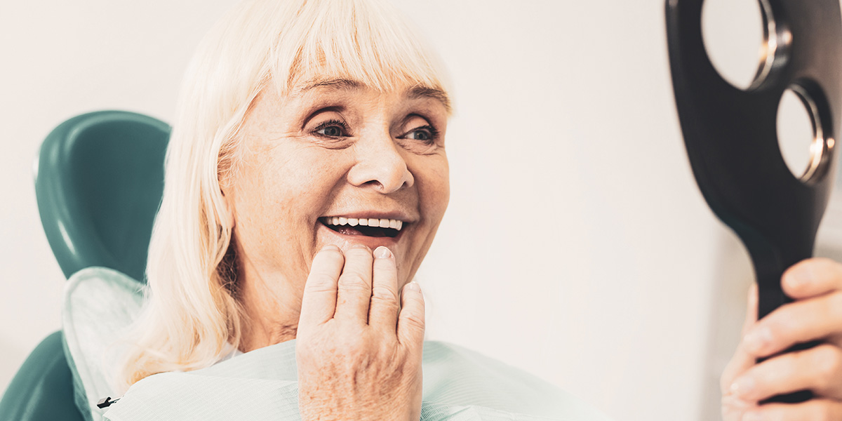 older woman looking at her teeth in the mirror